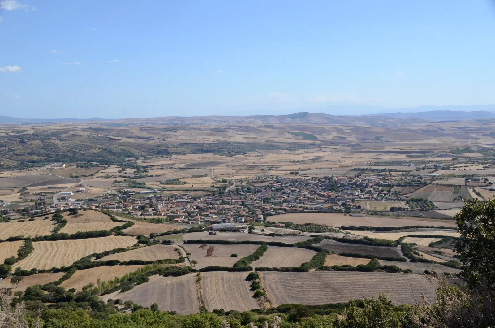 Vista dall'alto della Giara di Serri su un paese circondato da campi di cereali mietuti, filari di alberi e strade di campagna, con colline all'orizzonte
